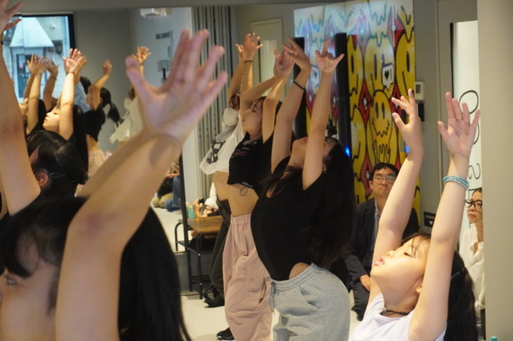 K-POPダンスワークショップで子どもたちが手を伸ばして踊っている様子。SAHOSHIHOレッスンの温かい空気と活気あるスタジオの雰囲気が伝わるシーン。