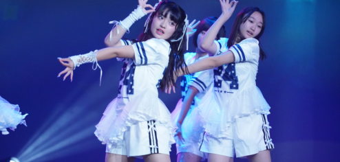 K-POPダンスショーケースイベント「Dance it UP」静岡開催のステージ写真。白のユニフォーム風衣装のチームが、息の合ったフォーメーションで踊っている。