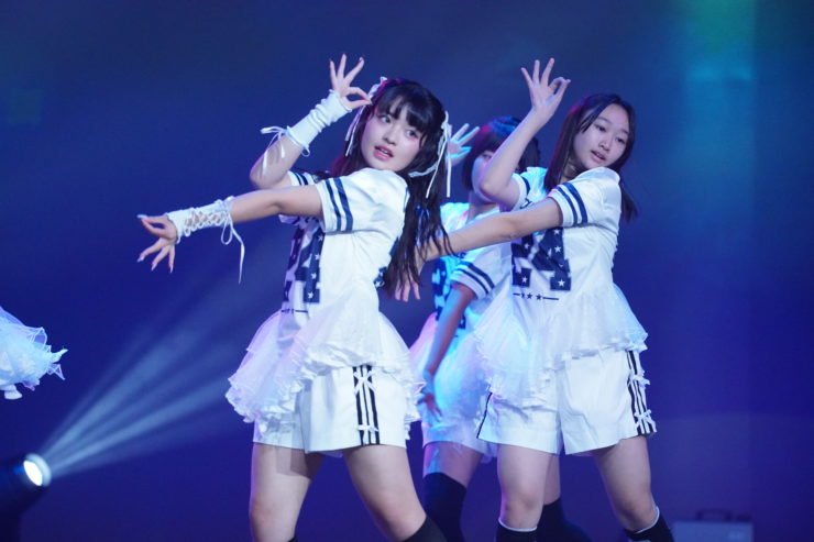 K-POPダンスショーケースイベント「Dance it UP」静岡開催のステージ写真。白のユニフォーム風衣装のチームが、息の合ったフォーメーションで踊っている。